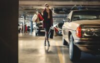 woman carrying shopping paper bags walking towards beige car inside parking lot